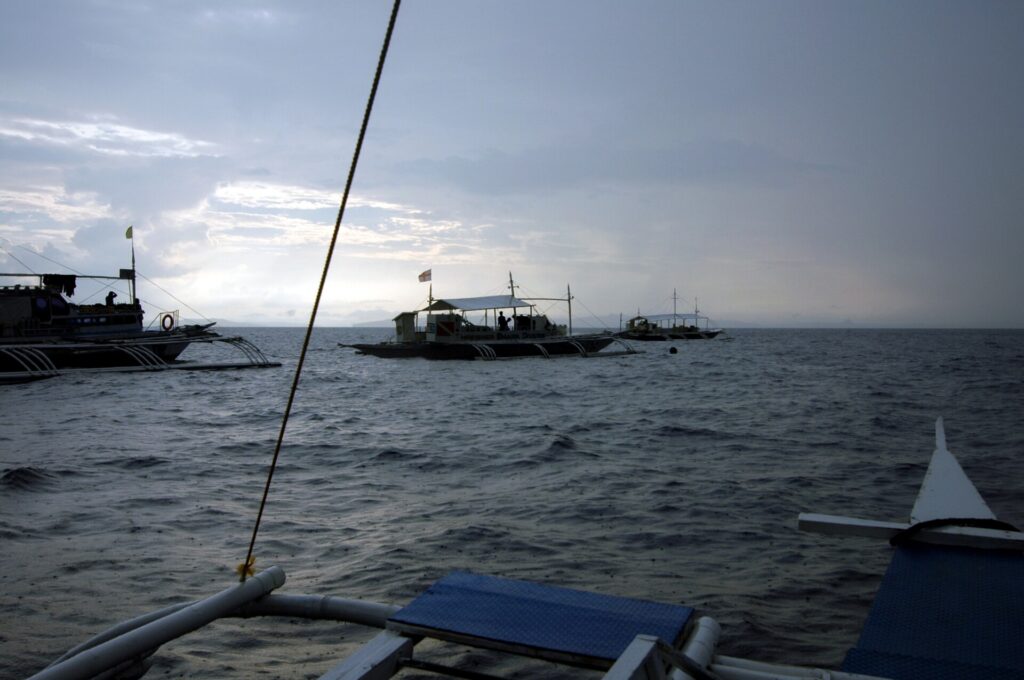 Drei Tauchbancas vor Anker an Monad Shoal unter grauem Morgenhimmel, vom Deck eines anderen Boots aus gesehen
