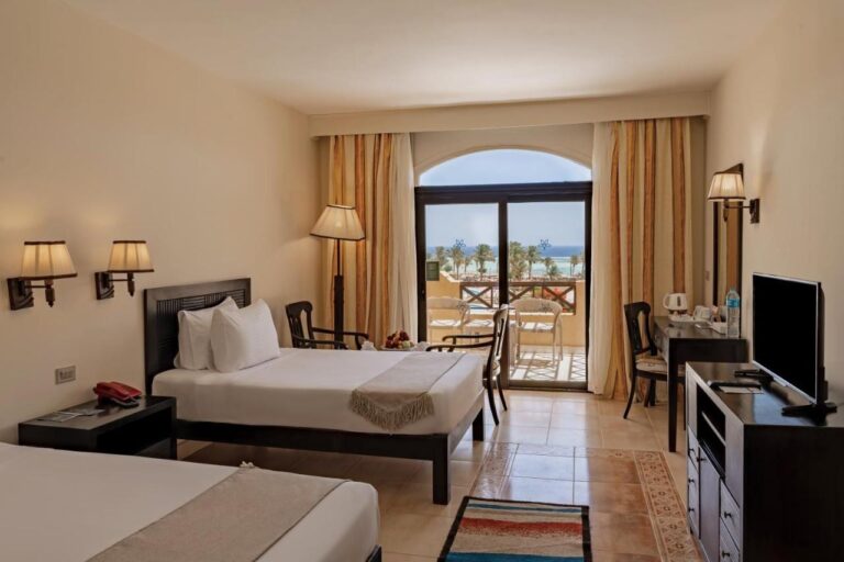 Ein Zweibettzimmer mit Fernseher, Schreibtisch und Balkon zum Meer