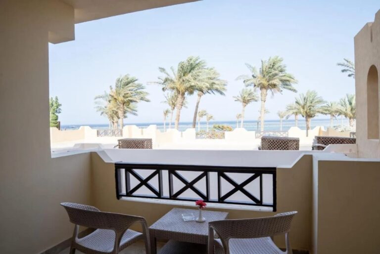 Ein Balkon mit zwei Stühlen und einem kleinen Tisch, mit Blick auf Palmen und Meer