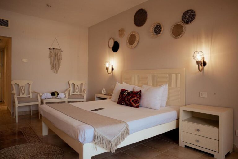 Ein Zimmer mit Doppelbett, geflochtenen Körben an der Wand und zwei weißen Stühlen
