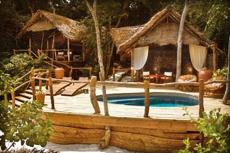 Zwei Bungalows mit Strohdach und eine Holzterrasse mit Becken und zwei Liegen