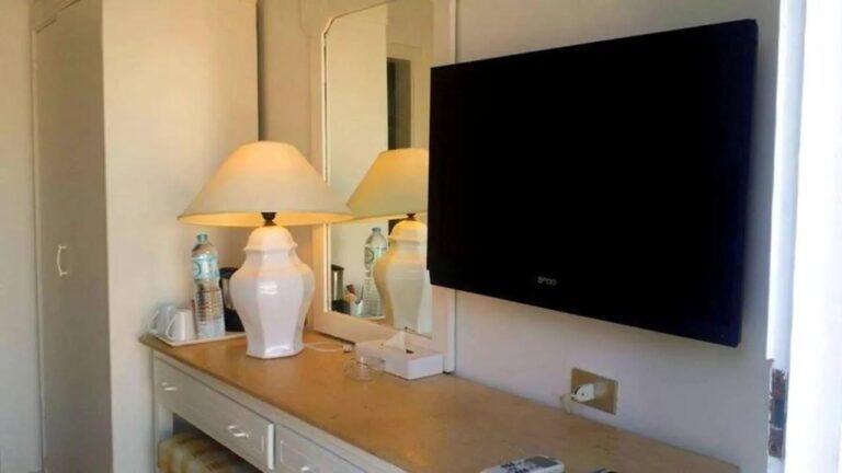 Eine Kommode mit weißer Lampe, ein Spiegel und ein Wandfernseher