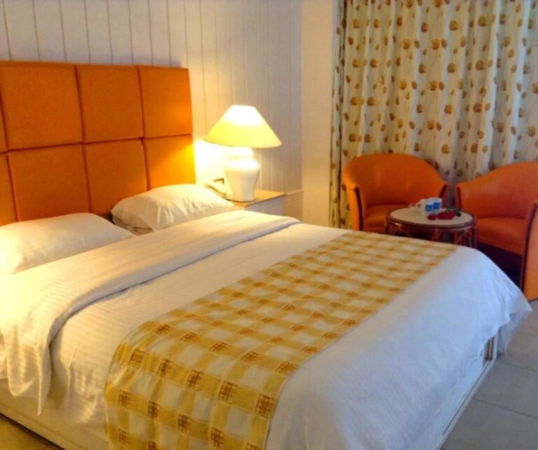 Ein Doppelbett mit orangefarbenem Kopfteil, zwei orangefarbenen Sesseln und einem kleinen runden Tisch