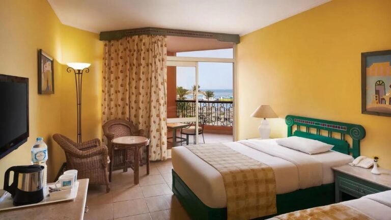 Ein Zimmer mit gelben Wänden, zwei Betten und einem Balkon zum Meer