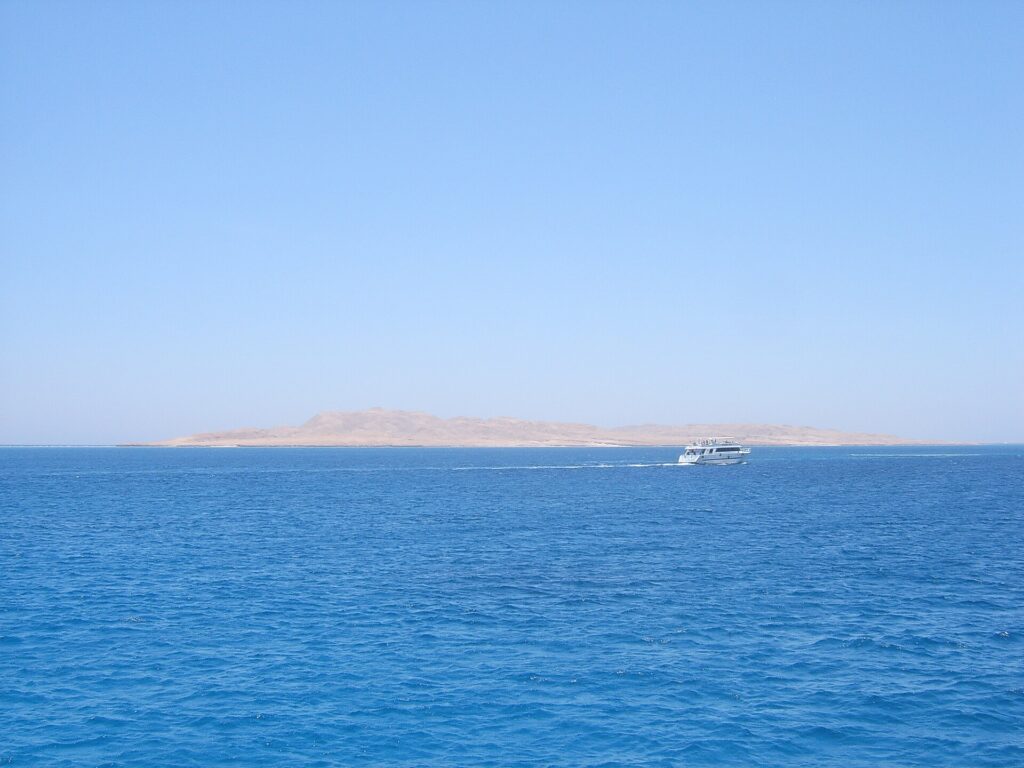Die flache Wüsteninsel Giftun Soraya vom Meer aus, davor fährt ein weißes Tauchboot vorbei