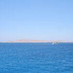 Die flache Wüsteninsel Giftun Soraya vom Meer aus, davor fährt ein weißes Tauchboot vorbei