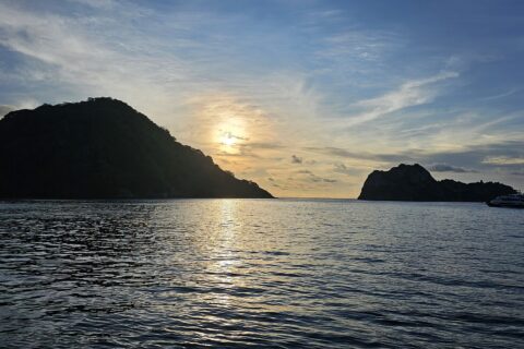 Die Kokosinsel im Gegenlicht bei Sonnenuntergang, rechts ein ankerndes Tauchsafarischiff, ruhige See