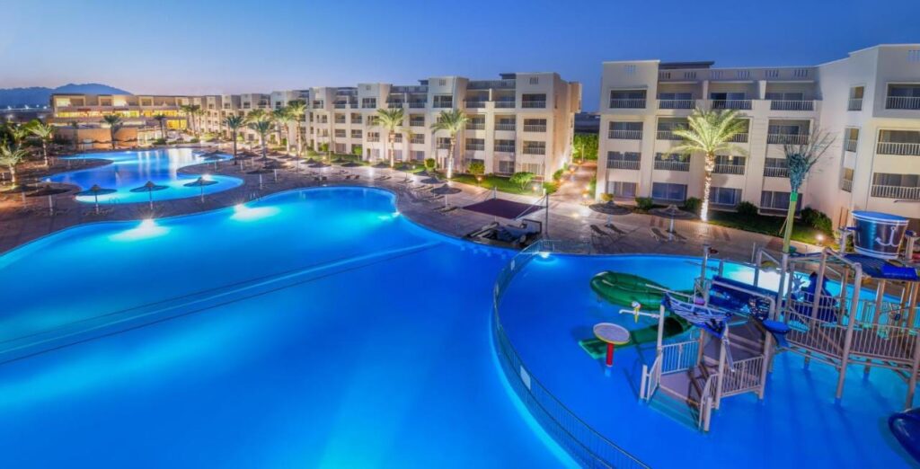 Die beleuchteten Pools des JAZ Soma Beach bei Einbruch der Dunkelheit, zwischen den Gebäuden und Palmen