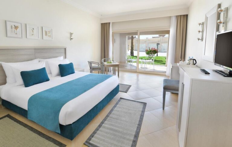 Ein Zimmer mit Doppelbett und hellen Möbeln, offen zu einer Terrasse und einer blühenden Rasenfläche