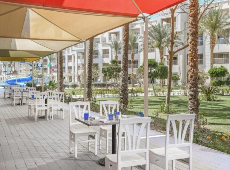Die Terrasse eines Restaurants unter Sonnensegeln, mit Blick auf den Garten und die Palmen