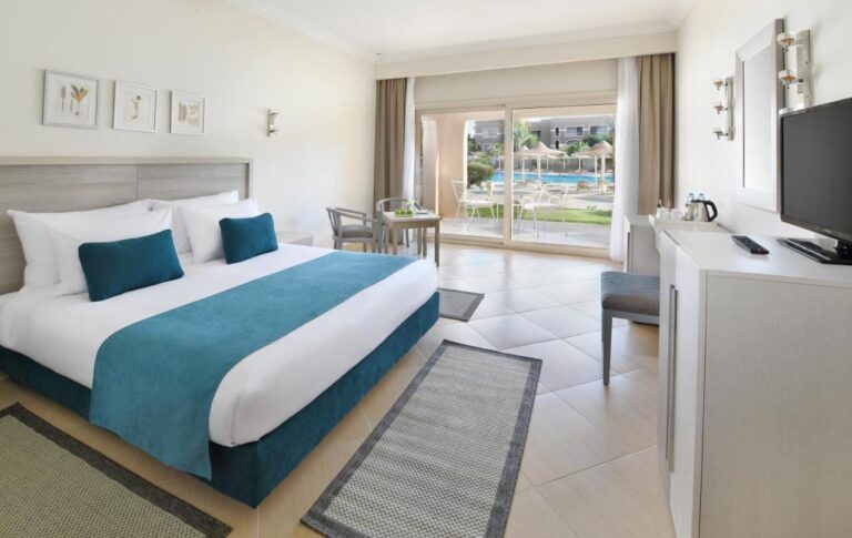 Ein Zimmer mit Doppelbett und hellen Möbeln, offen zu einer Terrasse mit Blick auf den Pool