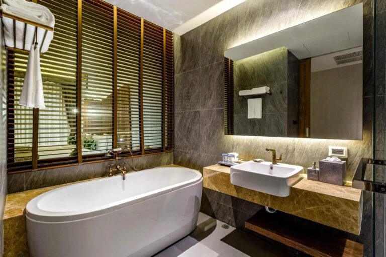 Eine ovale Badewanne vor hölzernen Fensterläden, neben einem Waschbecken