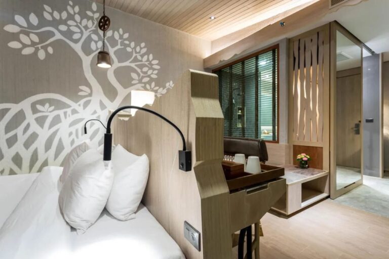 Ein Bett vor einer Wand mit einem aufgemalten weißen Baum, mit Leselampe