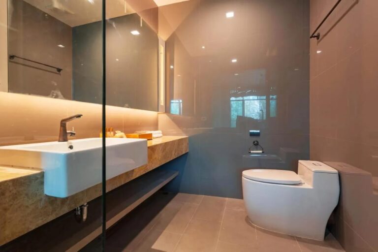 Ein Bad mit Waschbecken auf einer Marmorplatte, beleuchtetem Spiegel und Toilette
