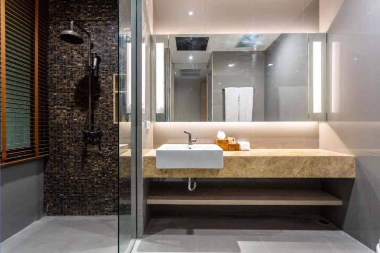 Eine Dusche an einer dunklen Mosaikwand, neben einem Waschbecken unter einem beleuchteten Spiegel