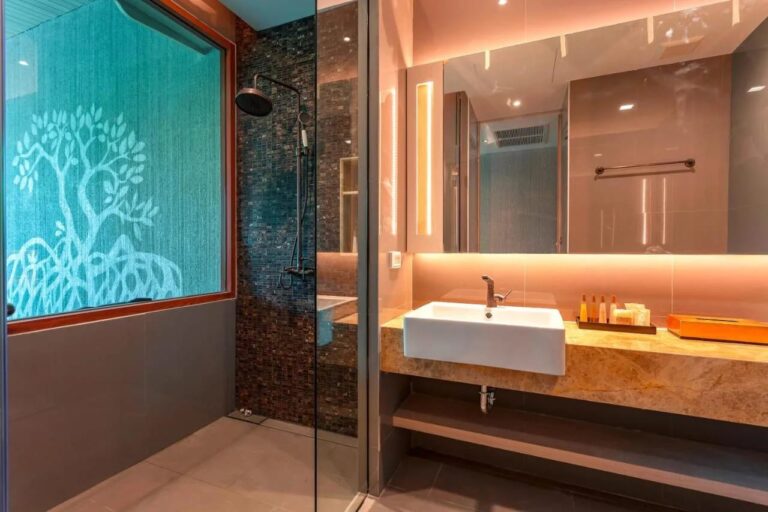 Eine Dusche hinter einer Glaswand, neben einem Fenster mit Baummotiv