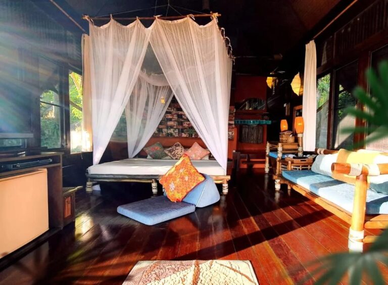 Das Bett unter dem Moskitonetz und die Sitzbank eines Cottages, von der Sonne beschienen