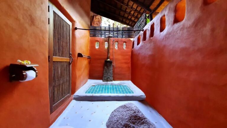 Ein halboffenes Bad mit orangefarbenen Wänden und einer Dusche auf türkisem Mosaikboden