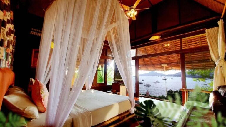 Ein Zimmer mit einem Bett unter einem Moskitonetz, offen zur Bucht und zu den Booten