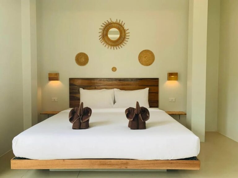 Ein Doppelbett mit Holzkopfteil, Handtuch-Elefanten und einem Sonnenspiegel aus Rattan