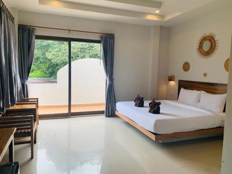 Ein Zimmer mit Doppelbett, einer Fensterfront zum Balkon und Holzsesseln