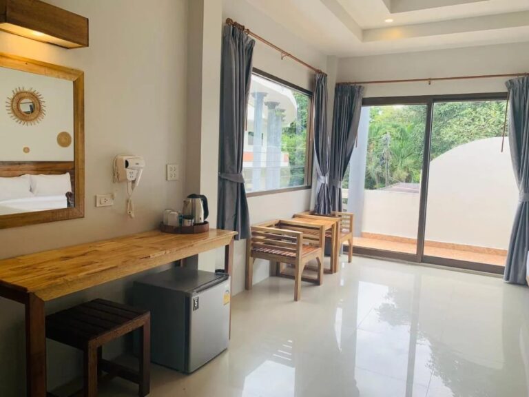 Ein Holzschreibtisch mit Wasserkocher und kleinem Kühlschrank, neben der Fensterfront zum Balkon