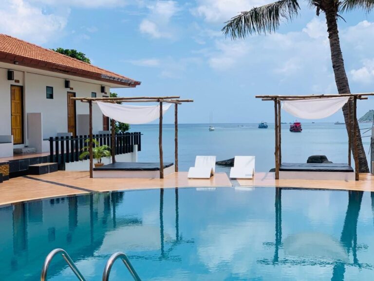 Der Pool mit Meerblick, mit zwei Betten unter einer Pergola und weißen Liegen