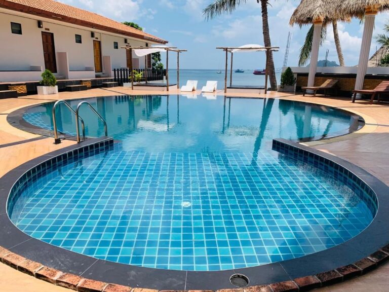 Der Pool mit blauen Fliesen, im Hintergrund das Meer und Boote