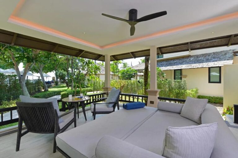 Eine überdachte Terrasse mit großem Tagesbett, zwei Sesseln und Deckenventilator