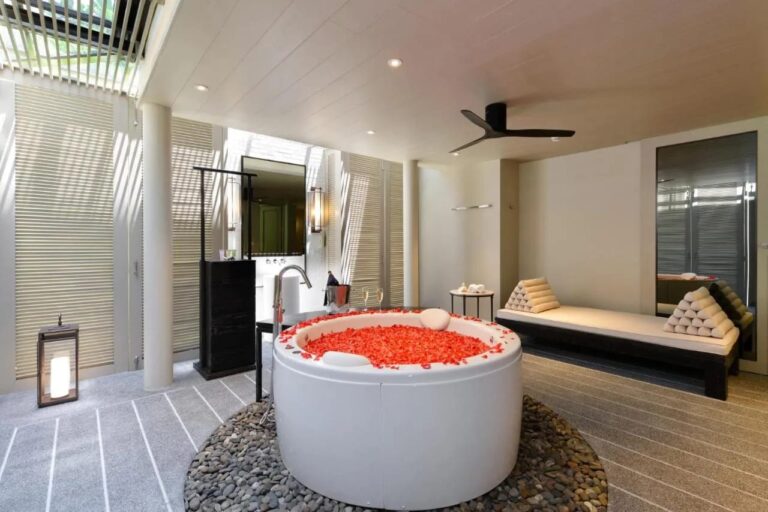 Eine runde Badewanne voller roter Blütenblätter, auf Kieselsteinen