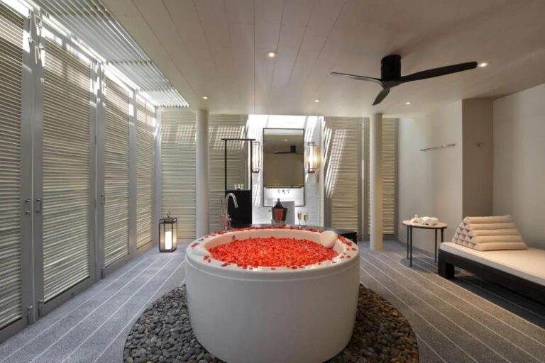 Ein Bad mit Lamellenfenstern, einer runden Badewanne in der Mitte und einer Sitzbank