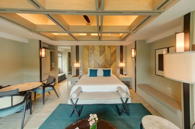 Ein Zimmer mit Doppelbett vor einer Holzwand im Fischgrätmuster, mit Bank und blaugrünem Teppich