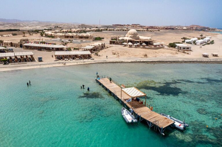 Das Marsa Shagra Village aus der Luft, mit Steg, zwei Zodiacs und dem Dorf am türkisfarbenen Wasser