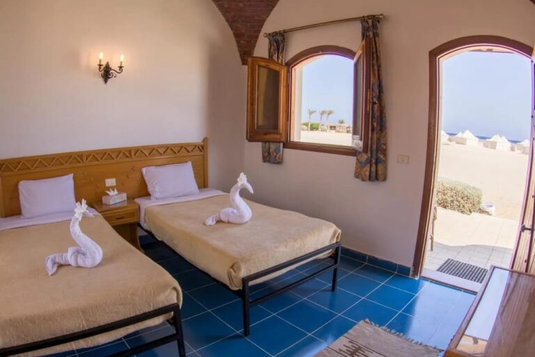 Ein Zweibettzimmer unter einem Ziegelgewölbe, die Tür offen zum Sand