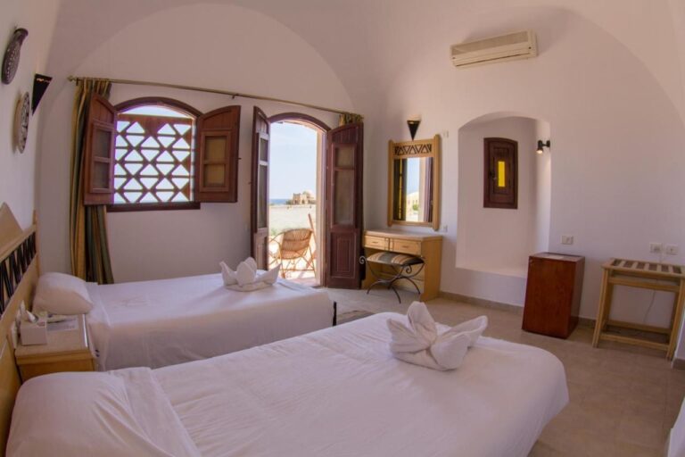 Ein Zweibettzimmer unter einem weißen Gewölbe, die Tür offen zu einer Terrasse und zum Meer