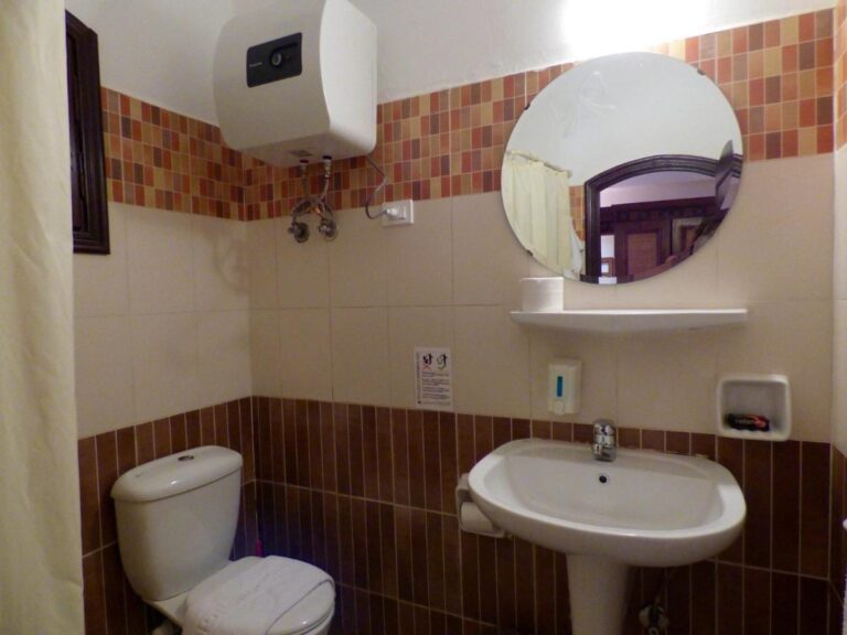 Ein Bad mit Waschbecken, Toilette, rundem Spiegel und Boiler