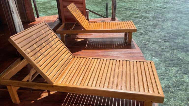 Zwei Holzliegen auf der Terrasse eines Bungalows, über klarem Wasser