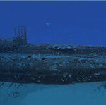 Unterwasserpanorama über die ganze Länge des Wracks der Rubis, aufrecht im Sand, der Turm in der Mitte, in blauem Wasser voller Fische.