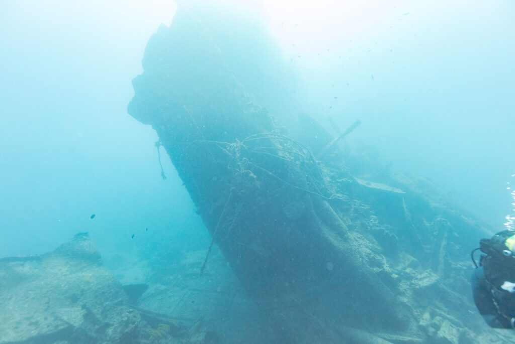 Das abgebrochene Heck der Thistlegorm ragt schräg ins Blaue, rechts ein Taucher