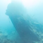 Das abgebrochene Heck der Thistlegorm ragt schräg ins Blaue, rechts ein Taucher