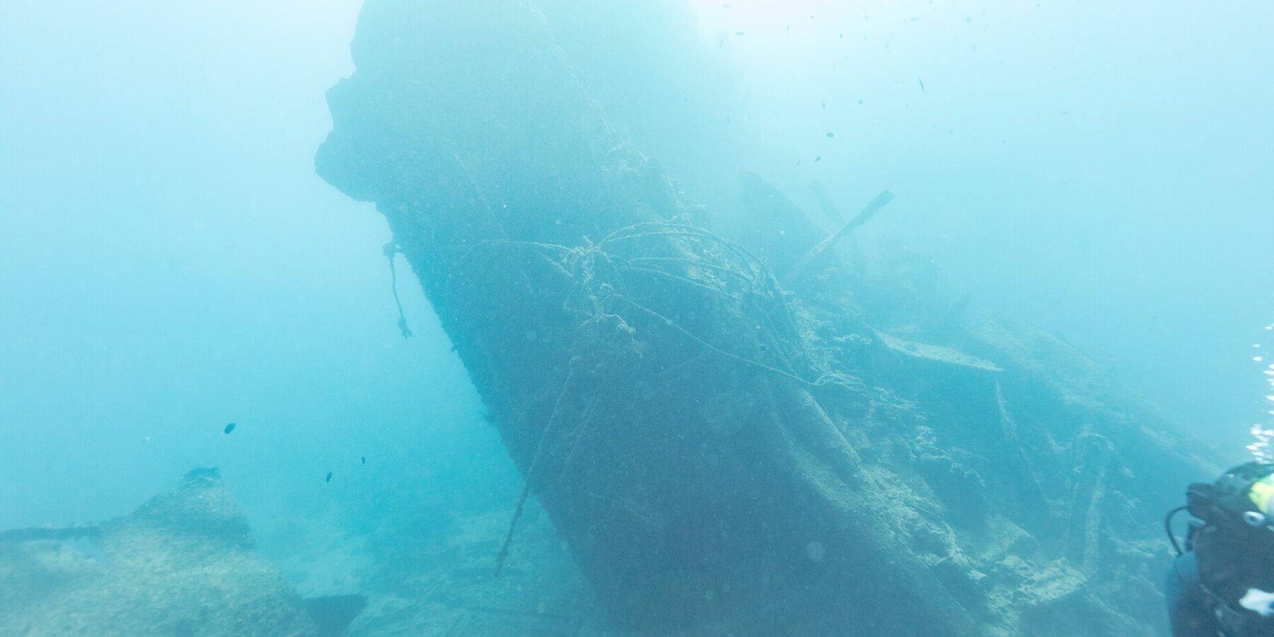 Das abgebrochene Heck der Thistlegorm ragt schräg ins Blaue, rechts ein Taucher