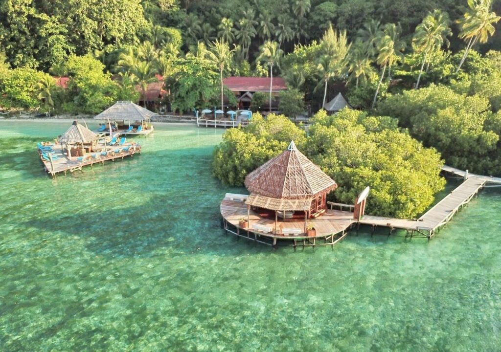 Luftaufnahme der Raja Ampat Dive Lodge mit ihren Stegen auf Stelzen und roten Dächern unter Palmen