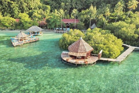 Luftaufnahme der Raja Ampat Dive Lodge mit ihren Stegen auf Stelzen und roten Dächern unter Palmen