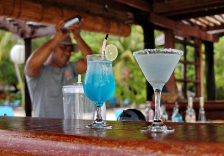 Zwei Cocktails, einer davon blau, auf der Holztheke der Bar, vor dem Barkeeper