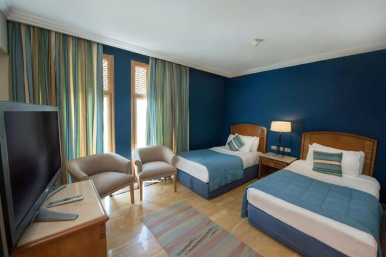 Ein Zweibettzimmer mit blauen Wänden und zwei Sesseln vor den Fenstern