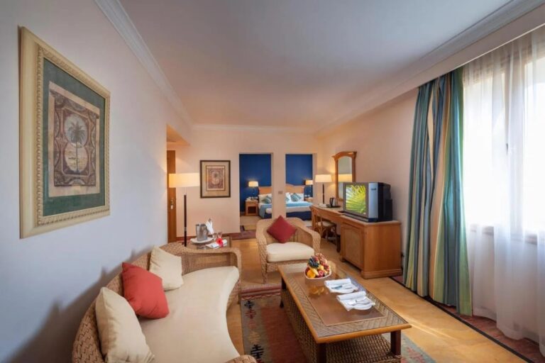 Ein Wohnbereich mit Rattanmöbeln, im Hintergrund ein Schlafzimmer mit blauer Wand