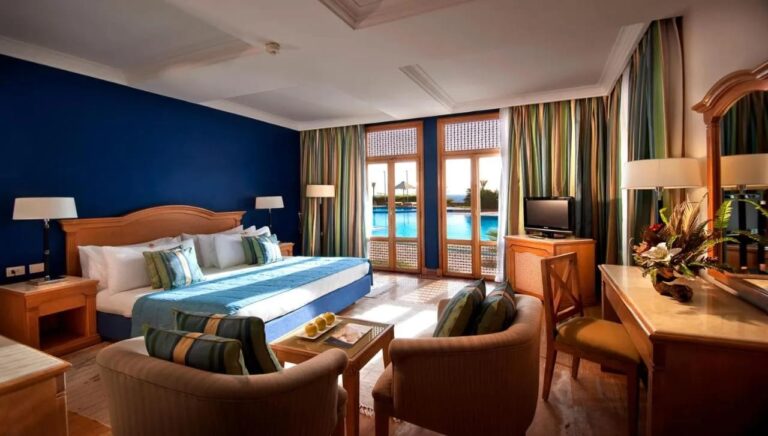 Ein Zimmer mit Doppelbett, blauer Wand und Fenstertüren zum Pool