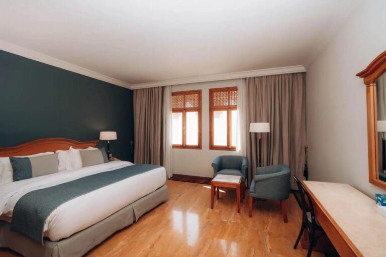 Ein Zimmer mit Doppelbett, dunkelgrüner Wand und zwei blauen Sesseln