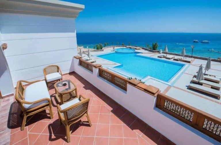 Eine Terrasse mit Rattanmöbeln über einem großen Pool und dem Roten Meer, im Reef Oasis Beach Resort