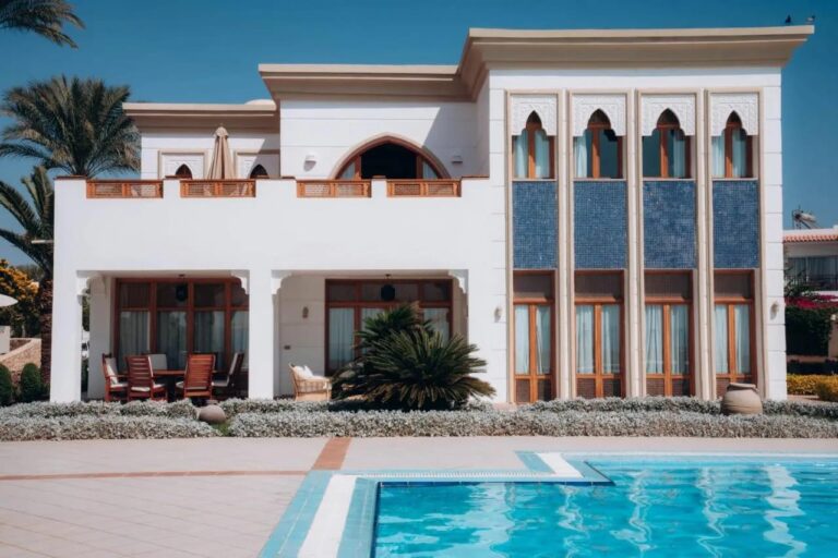 Ein weißes Gebäude des Reef Oasis Beach Resorts mit Bogenfenstern und blauen Mosaikfeldern, vor einem Pool